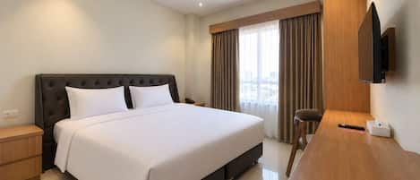A hotel room with a large bed, a desk, a chair, a television, and a window with curtains.