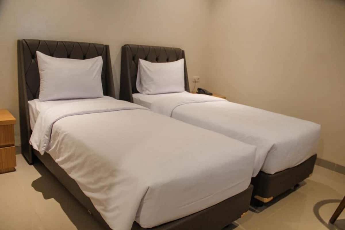 A hotel room with two beds, each with a headboard, a bedside table, and a wall socket.