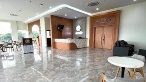 A spacious lobby with a reception desk, seating area, and a large wooden wardrobe.