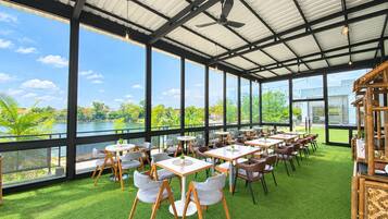 A restaurant with outdoor seating, large windows, and a view of a lake.