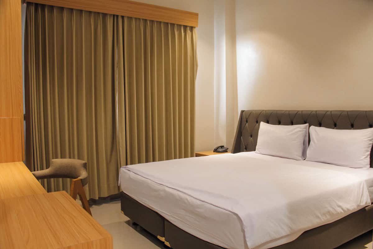 A hotel room with a bed, a wooden desk, a chair, and a curtain.