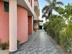 A hotel corridor with a tiled floor, a column, potted plants, and a palm tree. - Hotel Dhola Maru (Kota)