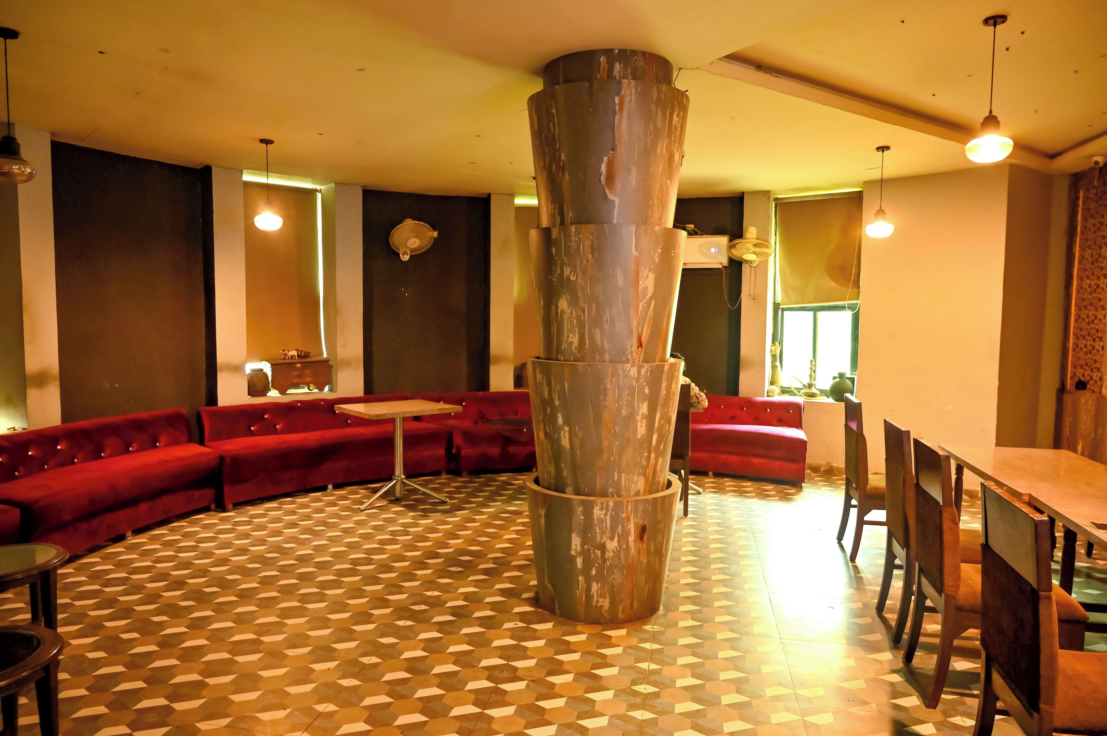 A room with a central column, red sofas, a patterned floor, and a dining area with chairs and a table.