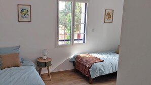 Ein Schlafzimmer mit zwei Betten, einem kleinen runden Tisch mit Lampe sowie zwei gerahmten Bildern an der Wand.