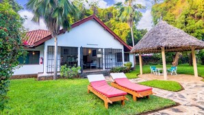 Ein Haus mit überdachter Terrasse, zwei Liegestühlen und einem strohgedeckten Dach.