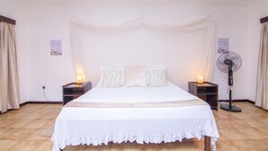 Ein Schlafzimmer mit einem Bett, zwei Nachttischen, einem Standventilator und Vorhängen.