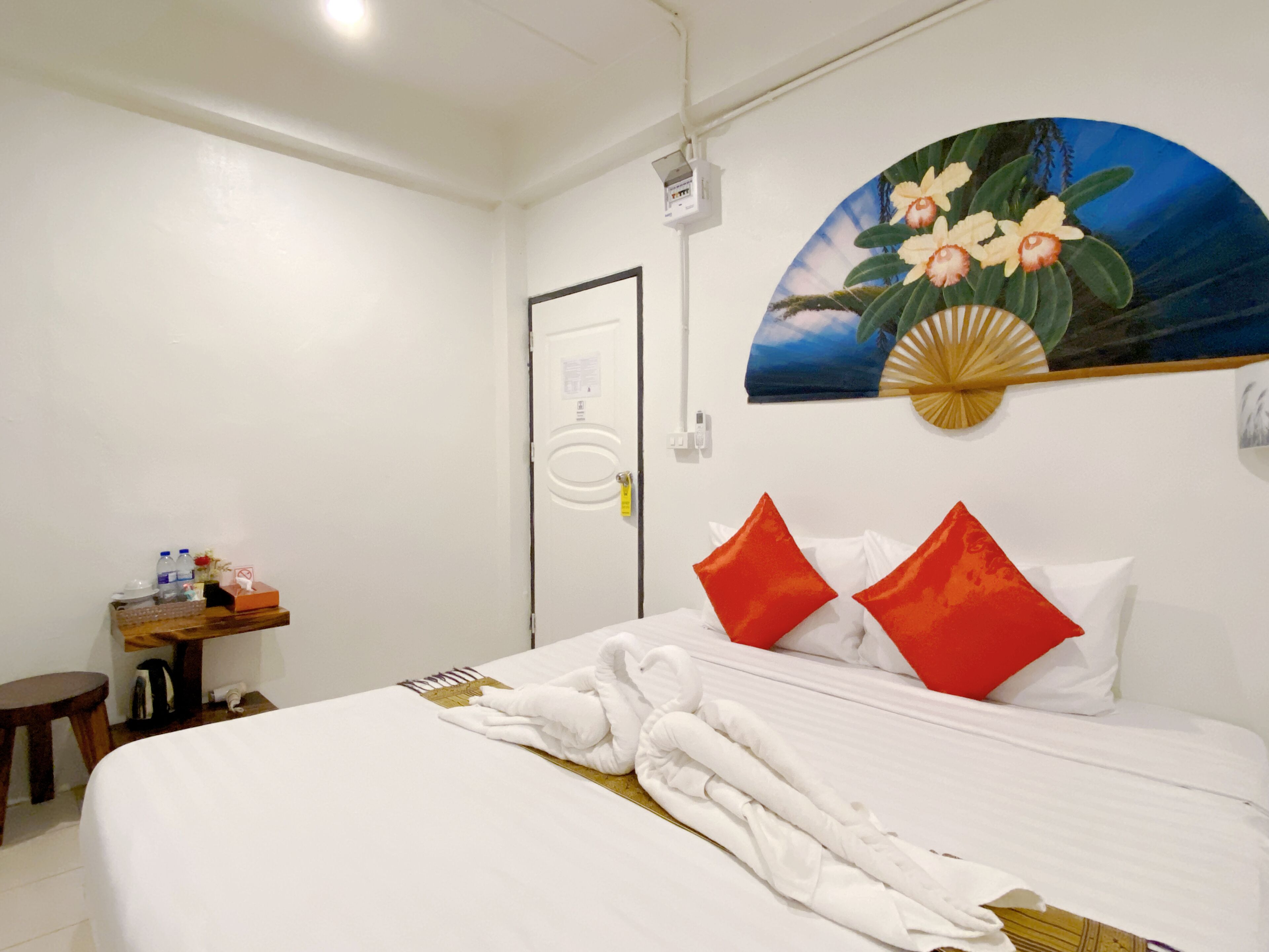 A hotel room with a neatly made bed, a small wooden side table with toiletries, and a painting of flowers on the wall.