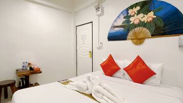 A hotel room with a neatly made bed, a small wooden side table with toiletries, and a painting of flowers on the wall.