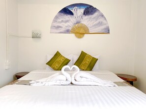 Habitación de hotel con cama, dos almohadas, ventilador de pared y una escultura de toallas.