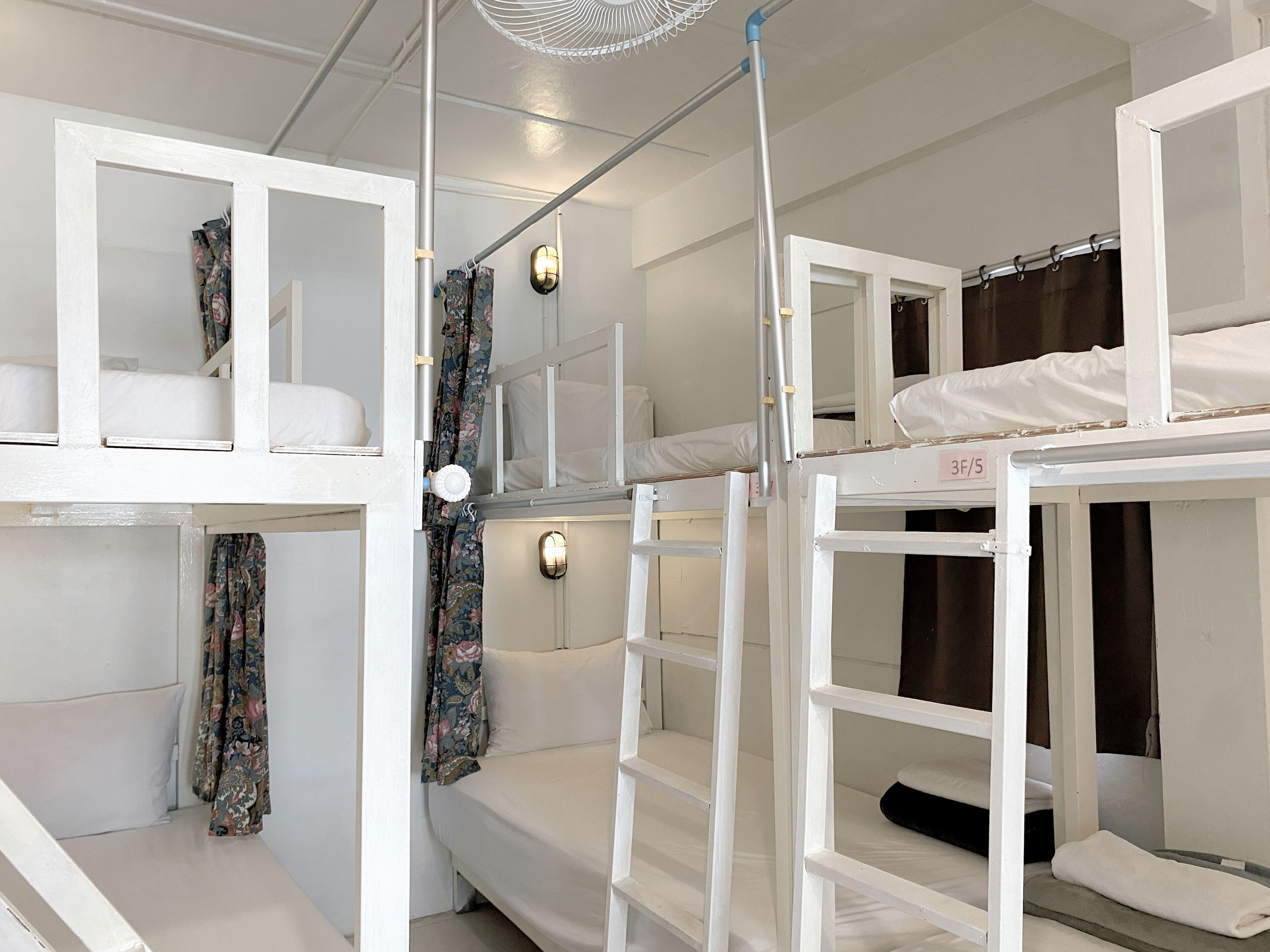 A dormitory-style room with bunk beds, a ceiling fan, and a wall-mounted light fixture.