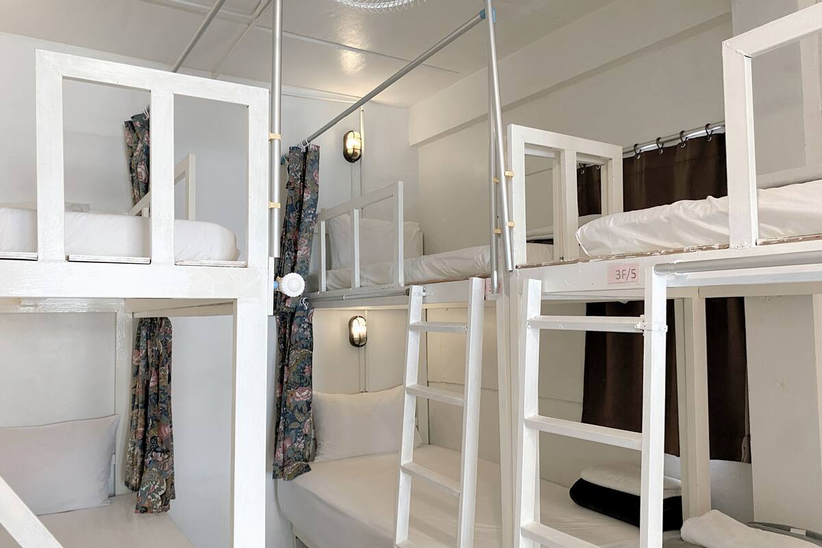 A dormitory-style room with bunk beds, a ceiling fan, and a wall-mounted light fixture.