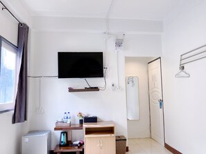 Habitación de hotel compacta con televisor de pantalla plana, kitchenette pequeña, ducha y puerta con perchero.
