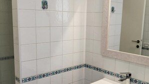 Une salle de bain avec des carreaux blancs, un lavabo et un miroir.