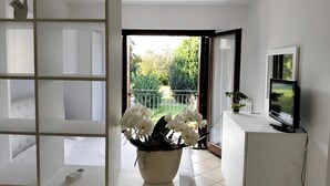 Un salon moderne avec une grande fenêtre, une console blanche, un téléviseur et une orchidée en pot.