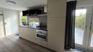 Eine moderne Küche mit Einbauherd, Backofen und Spüle, einer Schiebetür zum Balkon und einem Fenster mit Blick ins Grüne.