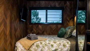 Un dormitorio con cama, ventana y televisor instalado en la pared.