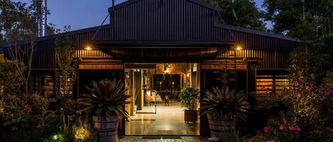 A building with a covered entrance, potted plants, and a pathway leading to the door.