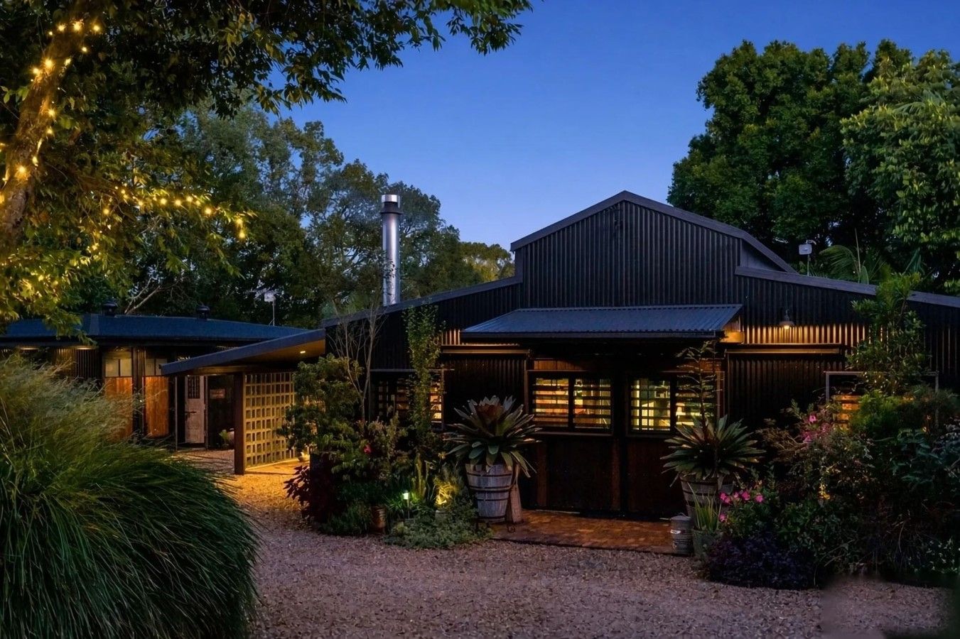 A modern house with a gravel driveway, surrounded by lush greenery and decorative lights.
