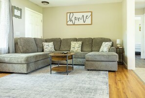 A living room with a sectional sofa, a coffee table, and a 'home' sign on the wall. - The Fieldstone Getaway (Ellsworth)