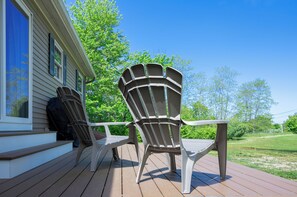 Eine Holzterrasse mit zwei Adirondack-Stühlen und einem Tisch.