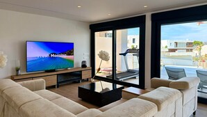 Ett modernt vardagsrum med en platt-TV, en beige soffa och ett soffbord i glas.