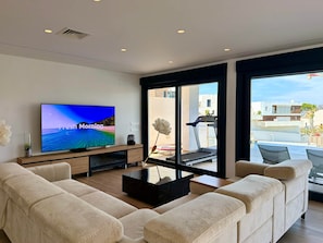 A modern living room with a flat-screen TV, beige sofa, and a glass coffee table. - Casa Montemar (Almuñécar)