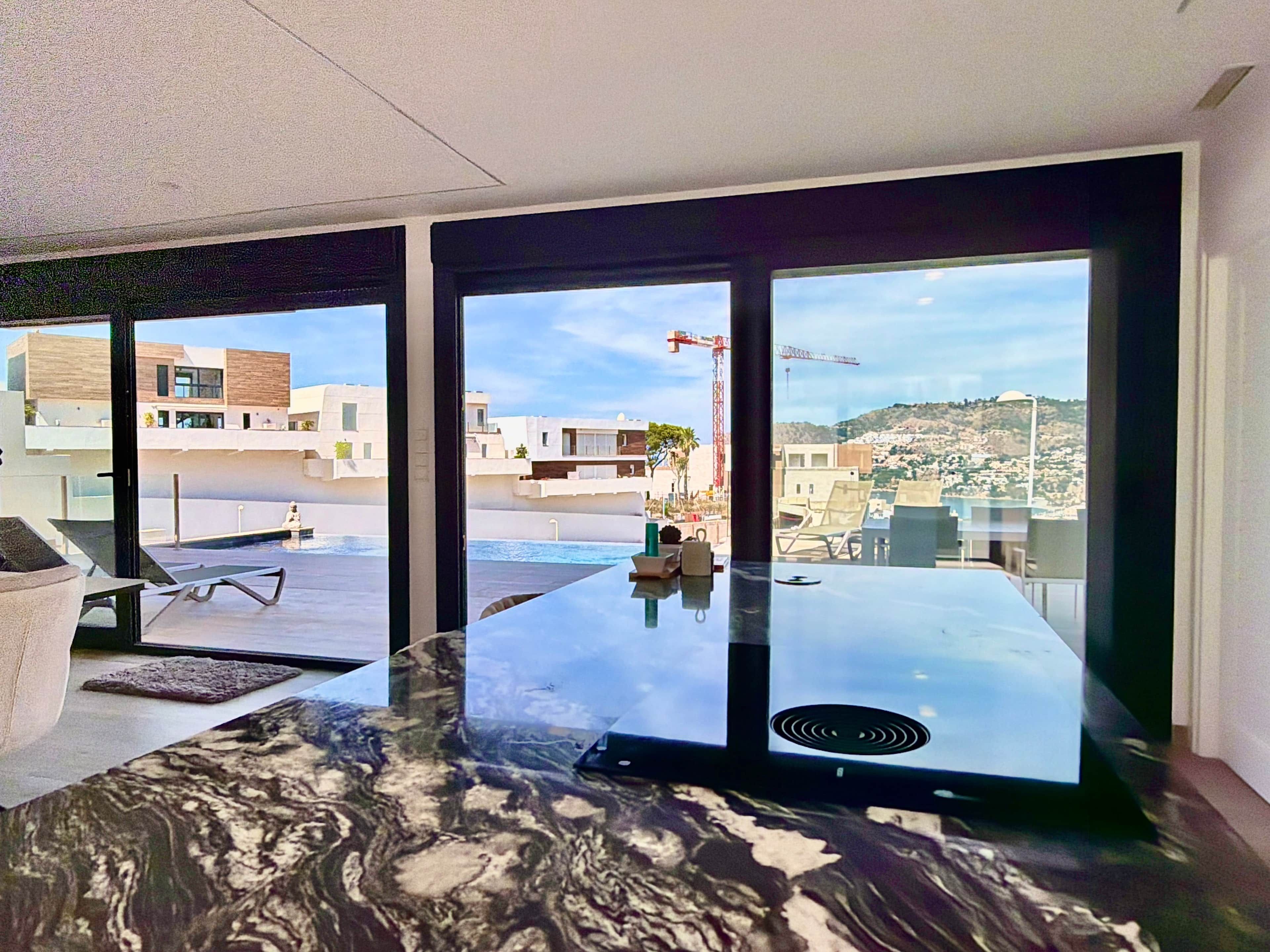 Una habitación moderna con un ventanal grande, una mesa de mármol y vistas a un paisaje urbano.
