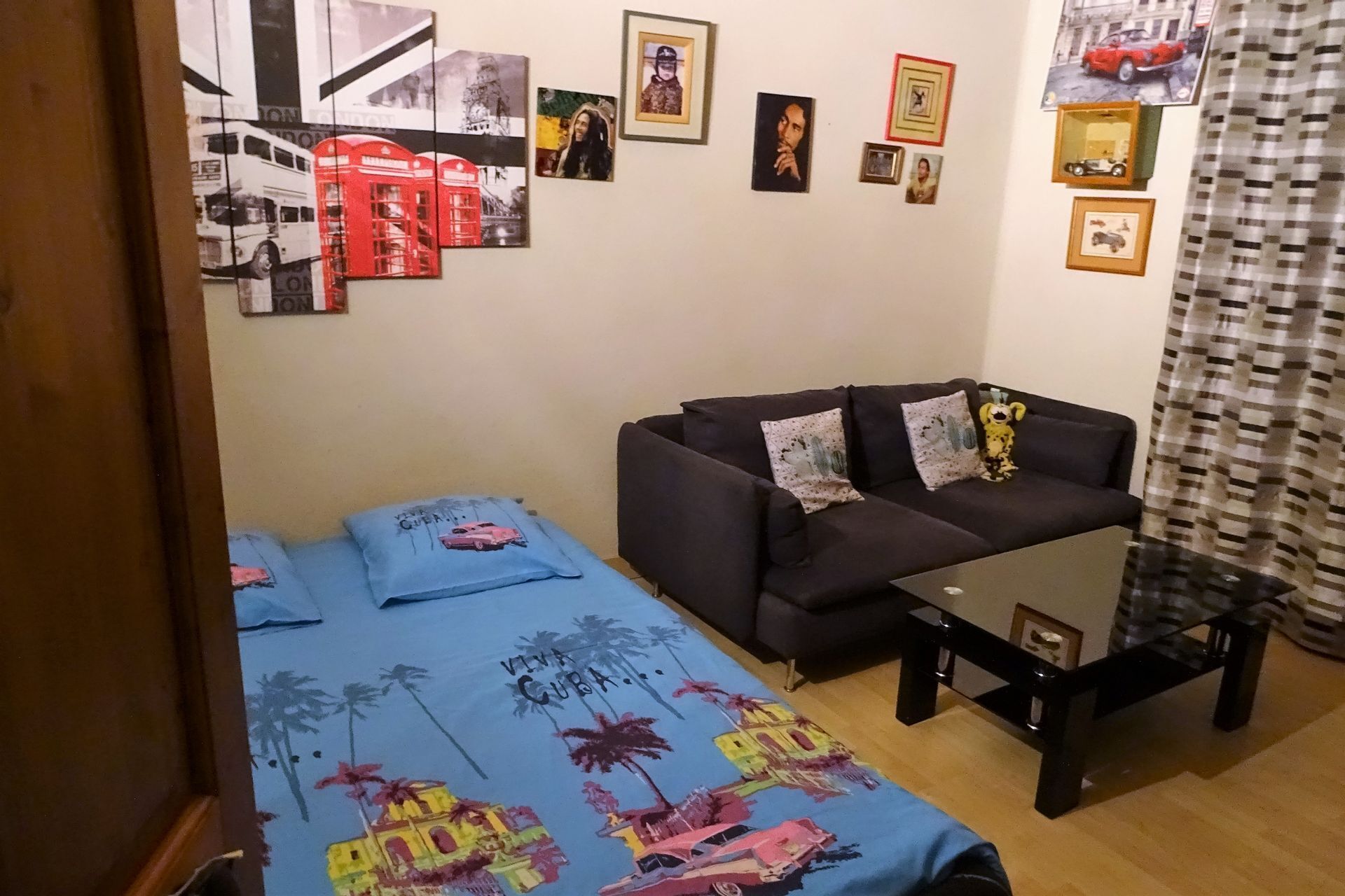 Ein Zimmer mit einer Couch, einem Bett mit tropischem Muster, einem kleinen Tisch und verschiedenen gerahmten Bildern an der Wand.