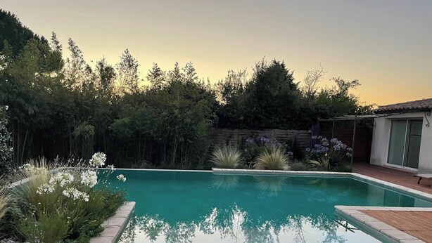 A rectangular swimming pool with a wooden deck in the foreground, surrounded by dense greenery and a house in the background. - L' ARC EN CIEL (Pujaut)