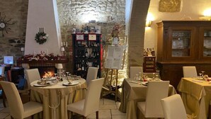 A restaurant with round tables, chairs, a fireplace, a stone wall, and a wine rack.