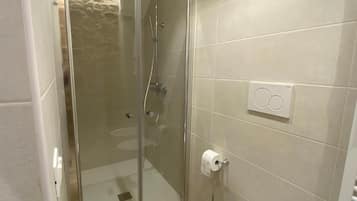 Un baño con ducha separada por mampara de vidrio, inodoro y un perchero para toallas.
