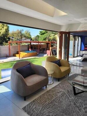 A modern living room with a large glass door leading to a backyard with a pool and a pergola. - 17 On Buffalo Sandton (Sandton)