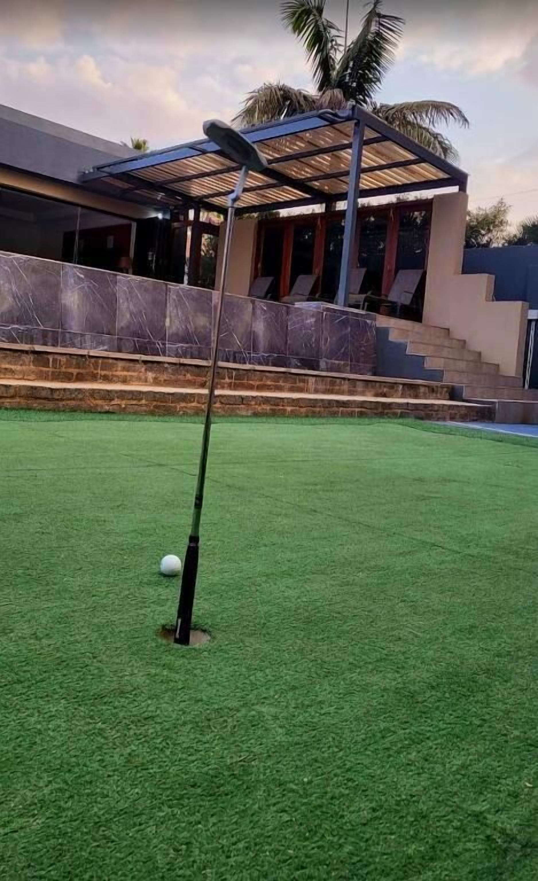 Een golfbaan met een putting green, een clubhuis en een palmboom op de achtergrond.