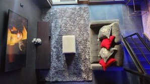 A room with a grey couch, a small white ottoman, a wall-mounted TV, and a skylight.