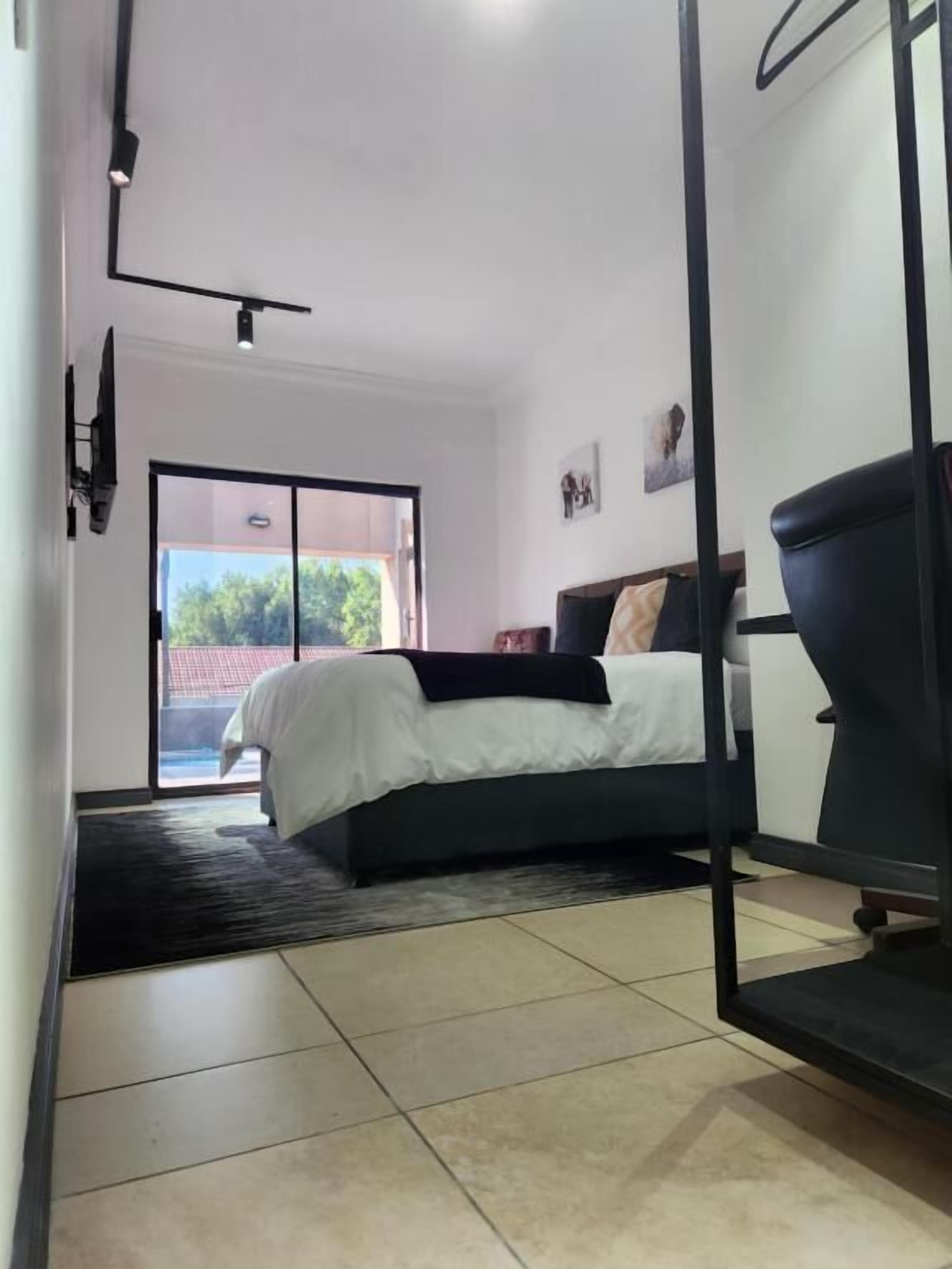 A bedroom with a bed, a chair, a desk, a door, and a view of the outdoors.