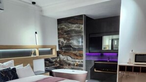 A modern hotel room with a large bed, a bathroom with a bathtub, a sofa, and a TV.