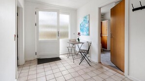 A hallway with a tiled floor, a door with frosted glass panels, a small table with a chair, and a wooden door on the right. - Sct. Knudsborg · Panorama apt 12E · Lillebælt (Middelfart)