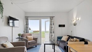 A modern living room with a sofa, armchair, and a dining table. - Sct. Knudsborg · Panorama apt 12E · Lillebælt (Middelfart)