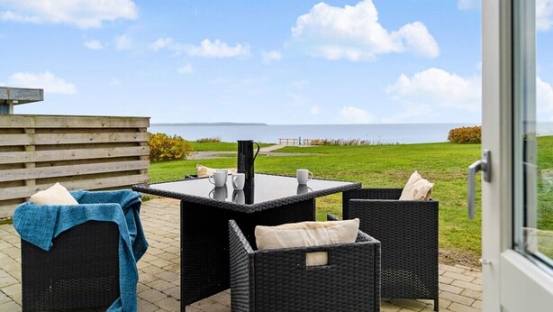 A patio with wicker furniture, a table, and a view of the sea. - Sct. Knudsborg · Panorama apt 12E · Lillebælt (Middelfart)