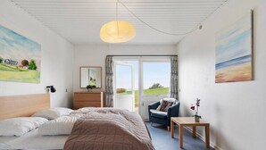 A bedroom with a bed, a chair, a small table, a lamp, and a view of the outdoors. - Sct. Knudsborg · Panorama apt 12E · Lillebælt (Middelfart)