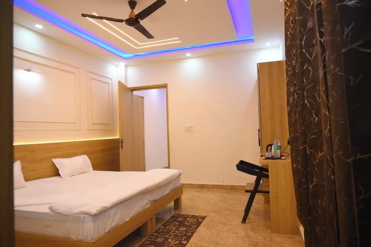 A bedroom with a bed, a desk, a chair, a ceiling fan, and a patterned curtain.