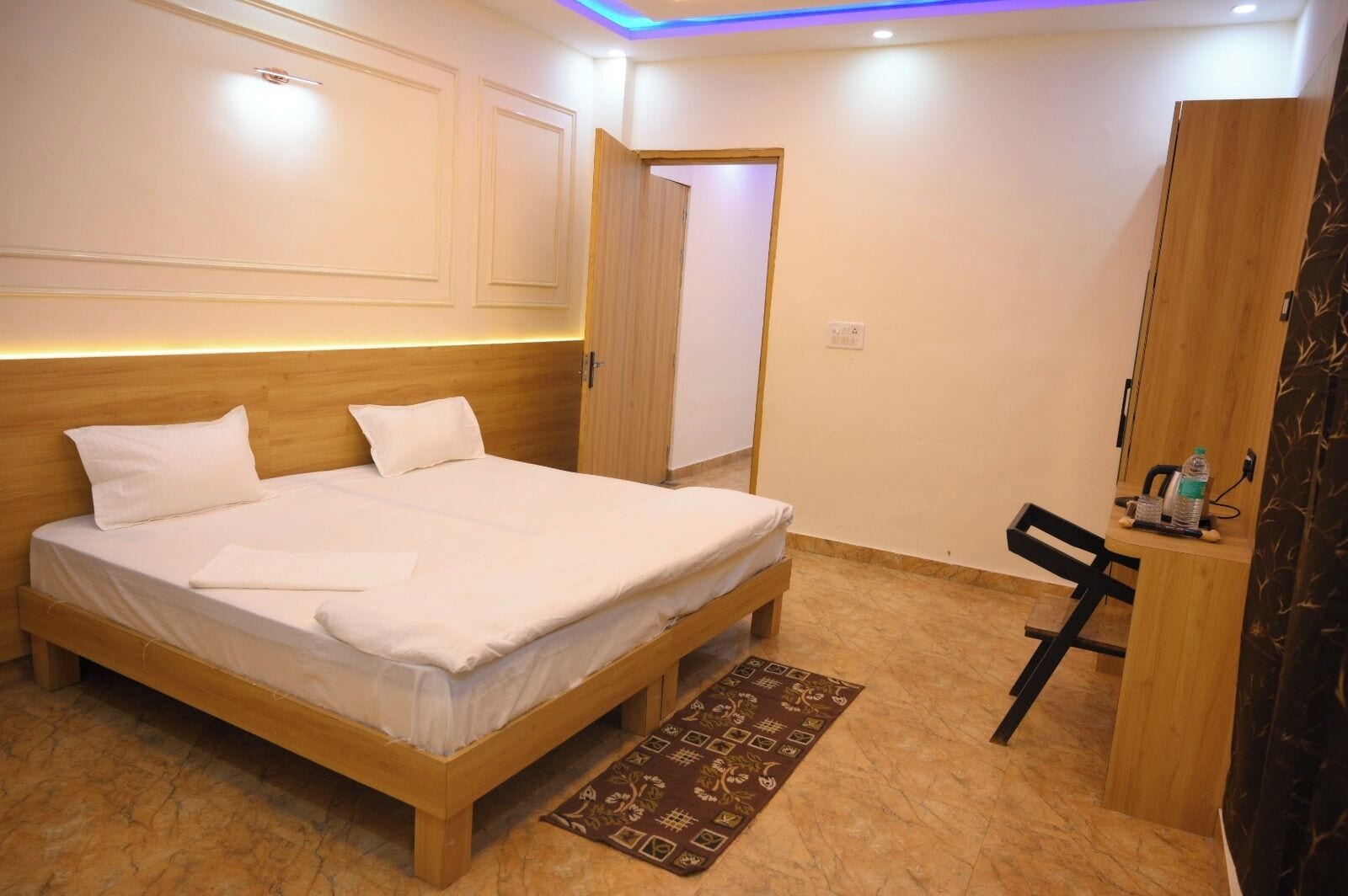 A hotel room with a wooden bed, a small desk with a chair, a mirror, and a door leading to another room.