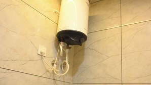Une salle de bain avec un chauffe-eau blanc fixé au mur, un porte-serviettes et un sol carrelé avec un motif imitant le marbre.