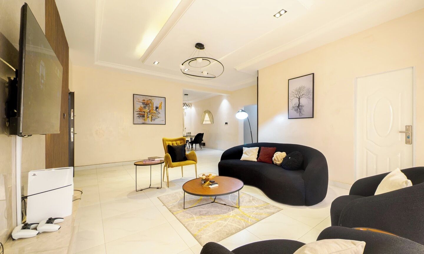 A modern living room with a flat-screen TV, a black sofa, a yellow armchair, and a coffee table.