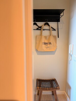 Ein Zimmer mit einer hölzernen Bank, einer aufhängbaren Tasche mit dem Aufdruck 'STRANDTAG' und einem schwarzen Regal.