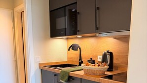 A modern kitchen with dark cabinets, a microwave, a sink, and a kettle. - Exclusive apartment with sea view in Haus Seeblick! - Lake view (Borkum)