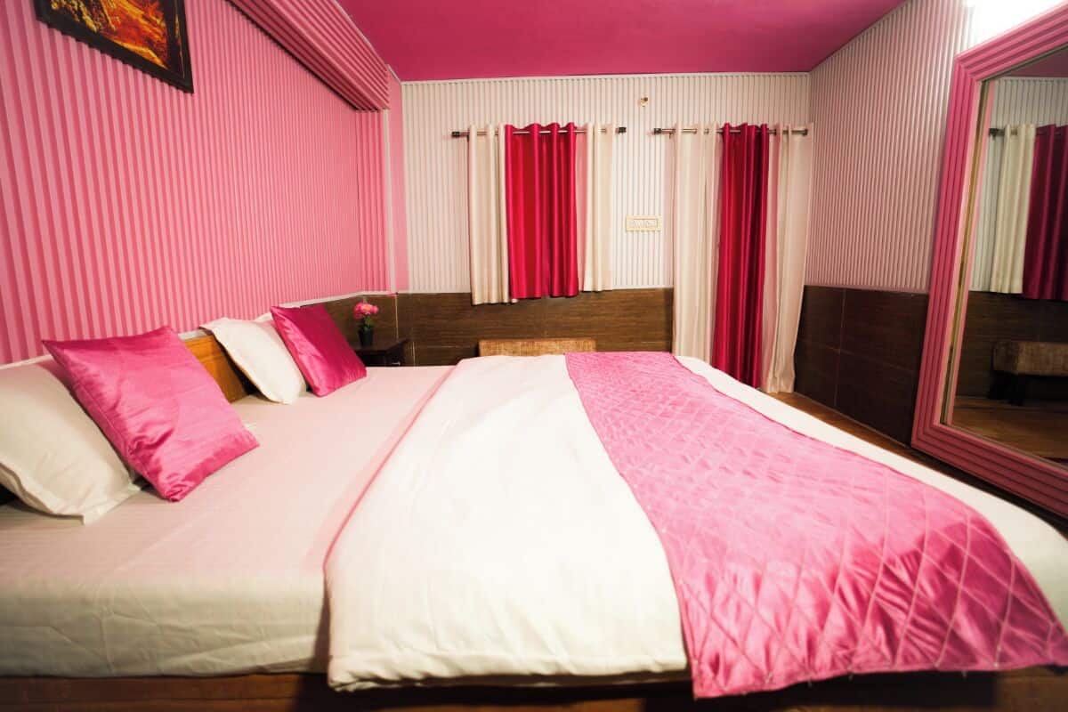 Una habitación de hotel con cama, cortinas rosadas, un espejo y una ventana con persianas.
