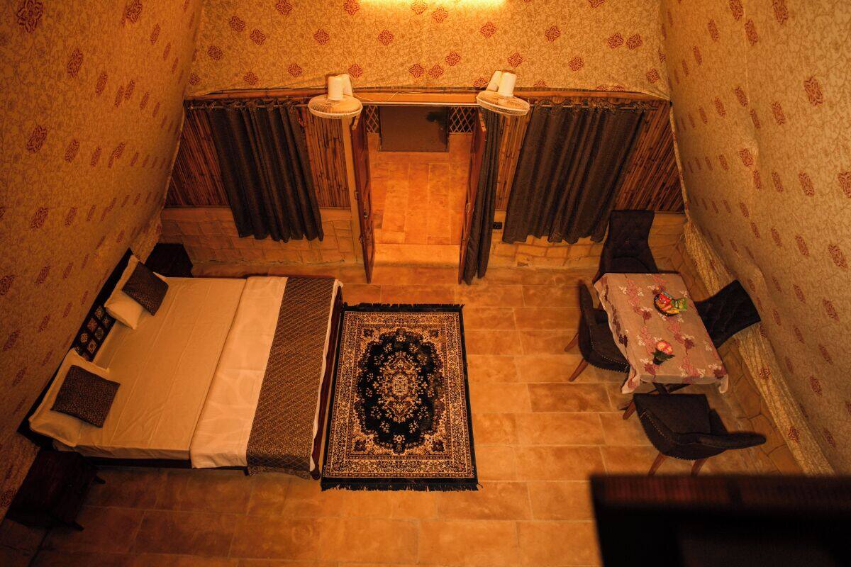 Una habitación pequeña y acogedora con una cama, una mesa y sillas, un tapete estampado y cortinas.