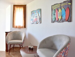 A room with two armchairs, a small table, and wall art depicting surfboards and a vintage car. - Relaxed family villa with garden, just steps from the beach in Fourka (Paliouri)