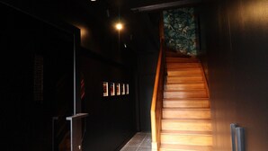 Un escalier avec des marches en bois menant à un étage supérieur, un mur sombre orné de tableaux encadrés et un sol carrelé.